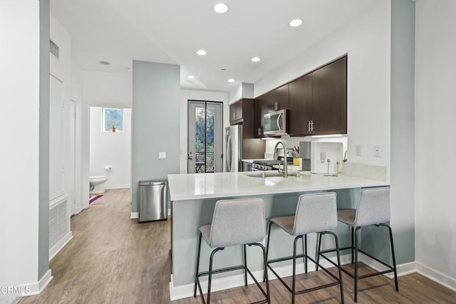 kitchen featuring stainless steel appliances, light countertops, light wood-style flooring, dark brown cabinets, and a peninsula