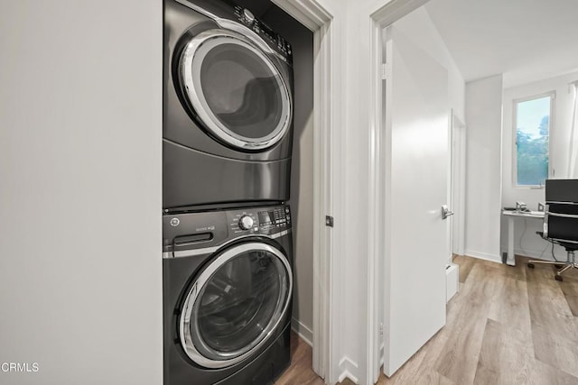 clothes washing area featuring laundry area, light wood finished floors, stacked washer / dryer, and baseboards