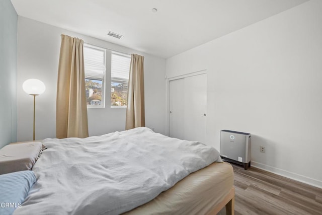 bedroom with a closet, visible vents, baseboards, and wood finished floors