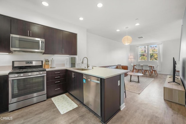 kitchen with light countertops, hanging light fixtures, appliances with stainless steel finishes, a sink, and a peninsula