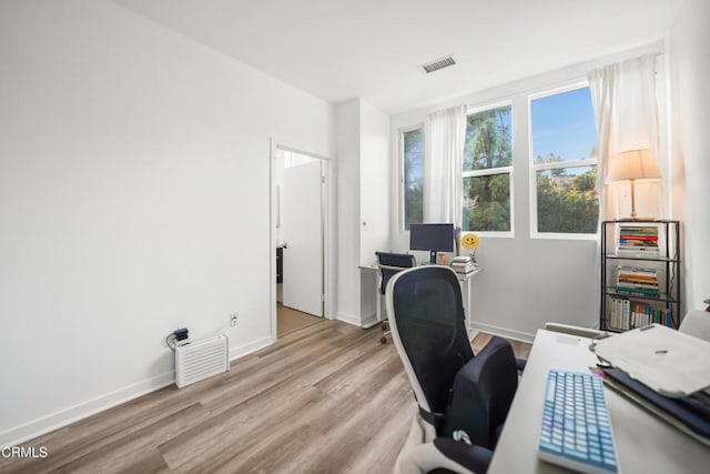 office space with light wood-type flooring, visible vents, and baseboards