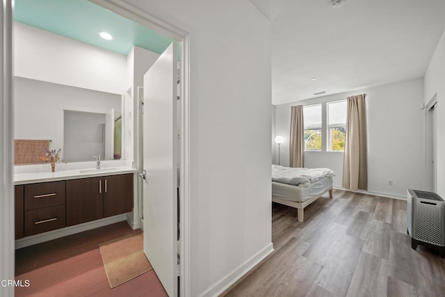 bedroom with a sink, ensuite bath, wood finished floors, and baseboards