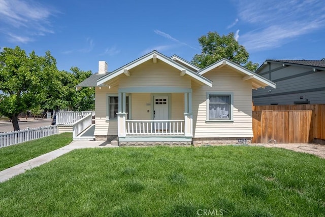 bungalow-style home with a porch, fence, a chimney, and a front lawn