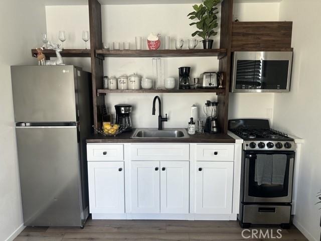 kitchen featuring dark countertops, stainless steel appliances, white cabinetry, open shelves, and a sink