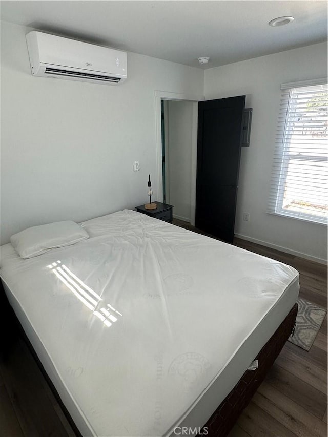 bedroom with a wall mounted air conditioner, wood finished floors, and baseboards