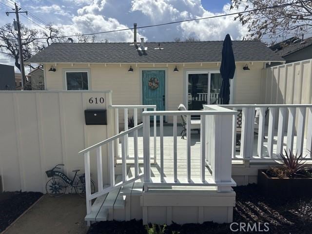 entrance to property with a shingled roof and fence