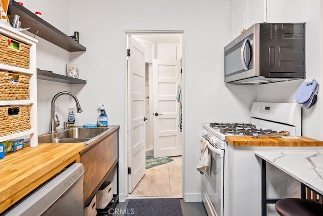kitchen featuring dishwasher, stainless steel microwave, white gas stove, open shelves, and a sink