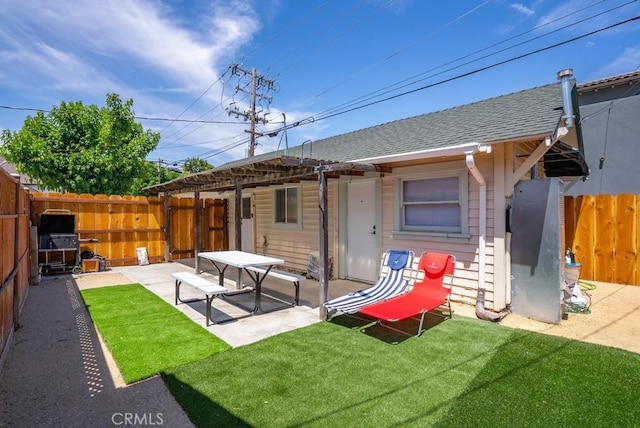 rear view of house featuring fence private yard, a shingled roof, a patio area, and a lawn