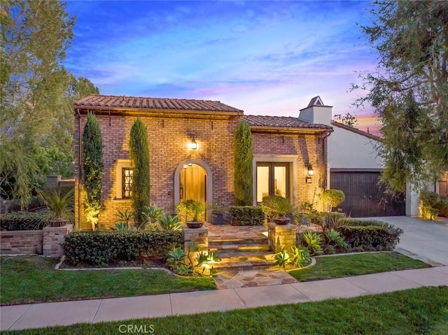 mediterranean / spanish-style house with a tile roof, brick siding, a chimney, concrete driveway, and a garage