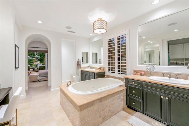 full bathroom featuring toilet, two vanities, a sink, visible vents, and a jetted tub