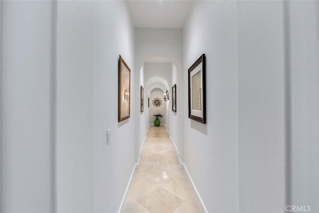 corridor with arched walkways, baseboards, and light tile patterned floors