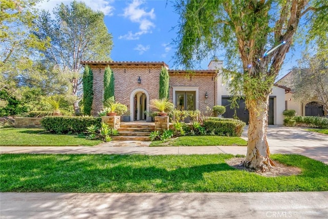 mediterranean / spanish-style house featuring brick siding, a chimney, concrete driveway, a garage, and a front lawn