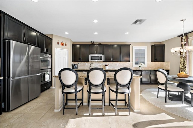 kitchen featuring visible vents, a kitchen island, light stone countertops, stainless steel appliances, and pendant lighting