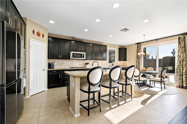 kitchen featuring visible vents, an island with sink, hanging light fixtures, light stone countertops, and stainless steel appliances