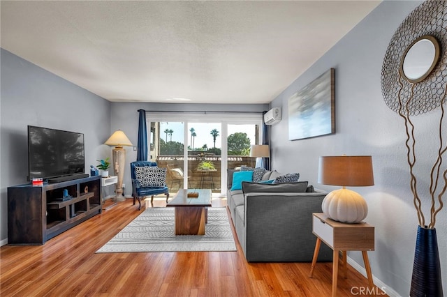 living area with a textured ceiling, a wall unit AC, wood finished floors, and baseboards