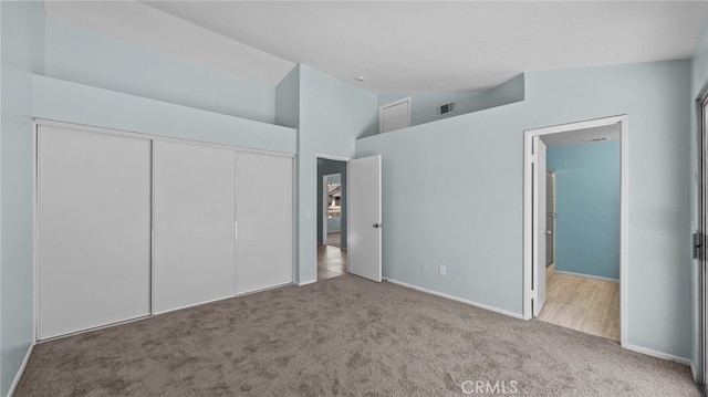 unfurnished bedroom with light carpet, visible vents, a closet, and lofted ceiling