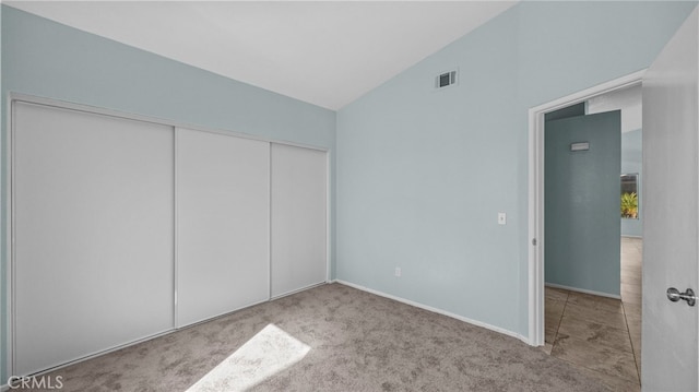 unfurnished bedroom featuring lofted ceiling, a closet, visible vents, light carpet, and baseboards