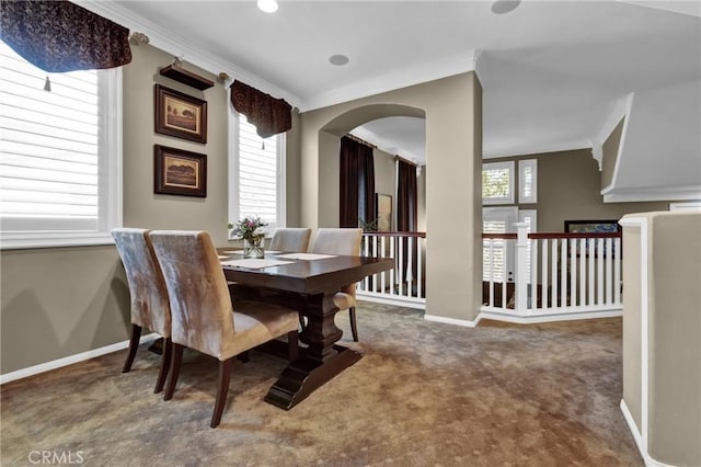 dining area with baseboards, ornamental molding, dark carpet, and arched walkways