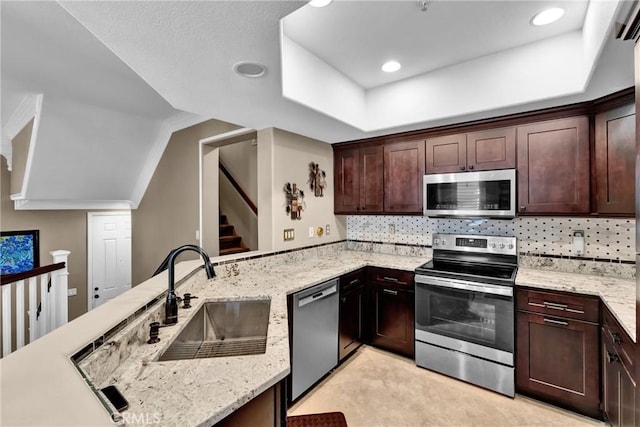 kitchen with tasteful backsplash, appliances with stainless steel finishes, a sink, light stone countertops, and a peninsula