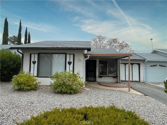 view of front of home featuring driveway, roof with shingles, an attached garage, and stucco siding