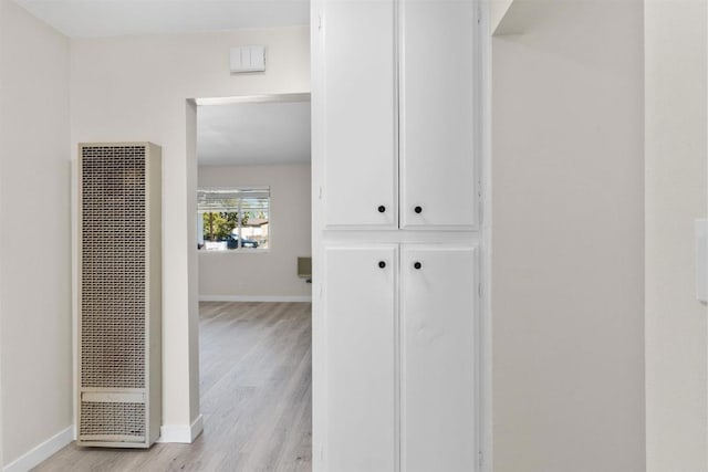 hall featuring light wood-type flooring, baseboards, and a heating unit