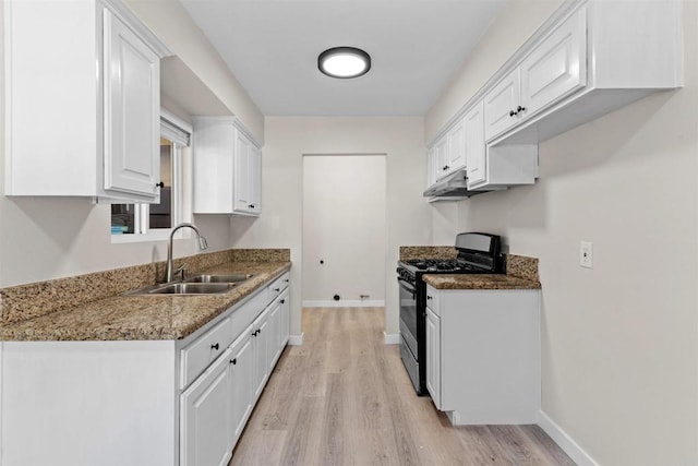 kitchen with dark stone counters, gas stove, a sink, and white cabinets