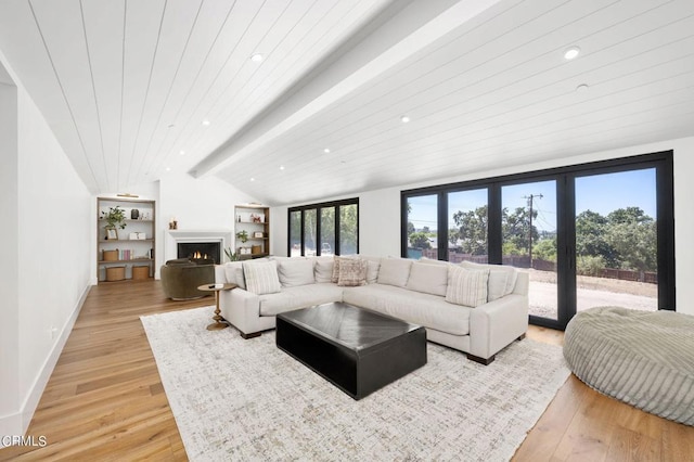 living room with a warm lit fireplace, baseboards, vaulted ceiling with beams, and light wood finished floors