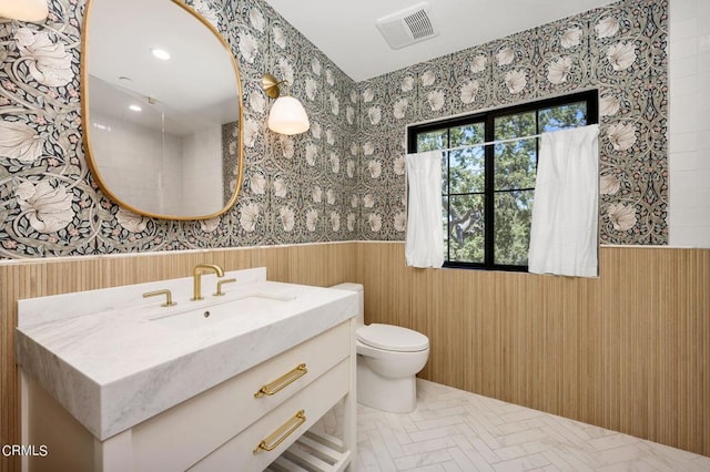 bathroom featuring toilet, a wainscoted wall, vanity, visible vents, and wallpapered walls