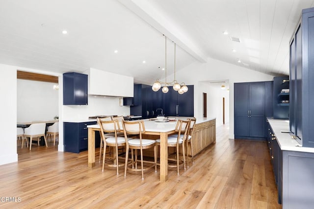 kitchen featuring blue cabinetry, a center island with sink, light countertops, and light wood finished floors