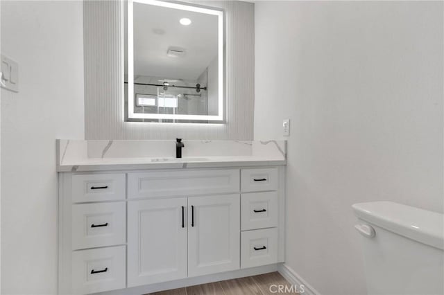 full bath with baseboards, toilet, wood finished floors, a shower with shower door, and vanity