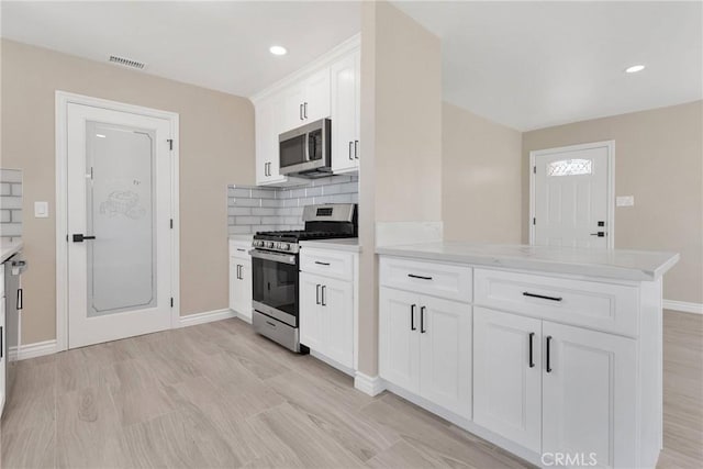 kitchen featuring tasteful backsplash, baseboards, a peninsula, stainless steel appliances, and white cabinetry