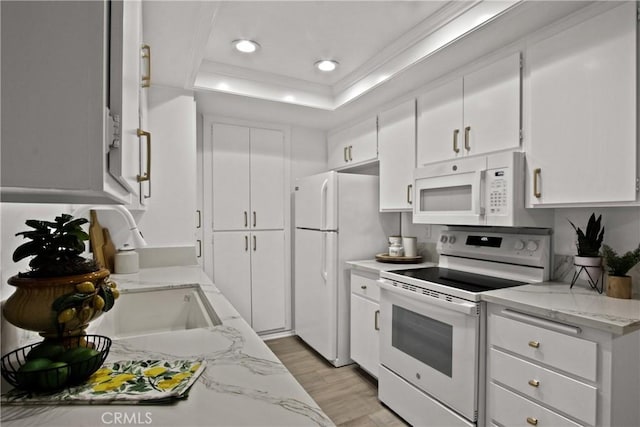 kitchen with a tray ceiling, white appliances, white cabinets, and light stone countertops