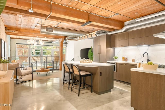 kitchen with a breakfast bar area, hanging light fixtures, light countertops, modern cabinets, and finished concrete floors