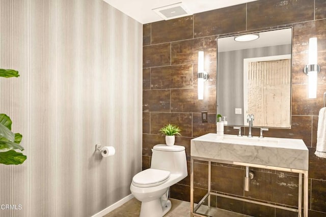 bathroom featuring a sink, tile walls, and toilet