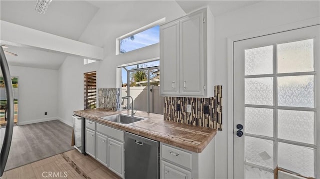 kitchen with lofted ceiling, a sink, backsplash, tile counters, and dishwasher