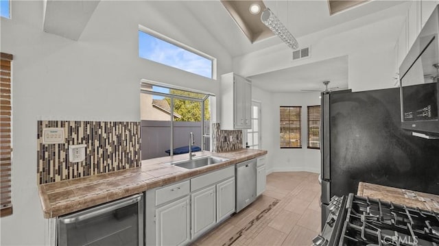 kitchen featuring tile countertops, visible vents, decorative backsplash, appliances with stainless steel finishes, and a sink