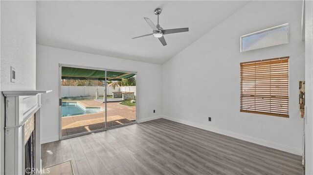 spare room featuring a fireplace with flush hearth, baseboards, vaulted ceiling, and wood finished floors