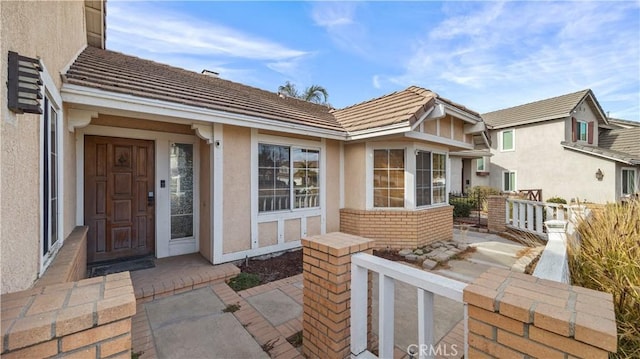 property entrance with stucco siding, a tile roof, and brick siding