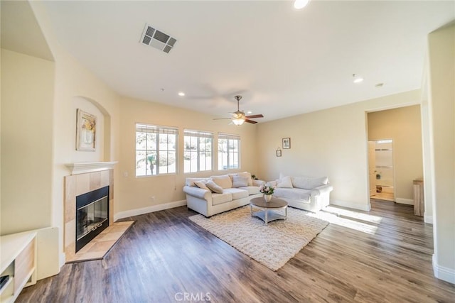 living area featuring baseboards, visible vents, a tiled fireplace, and wood finished floors