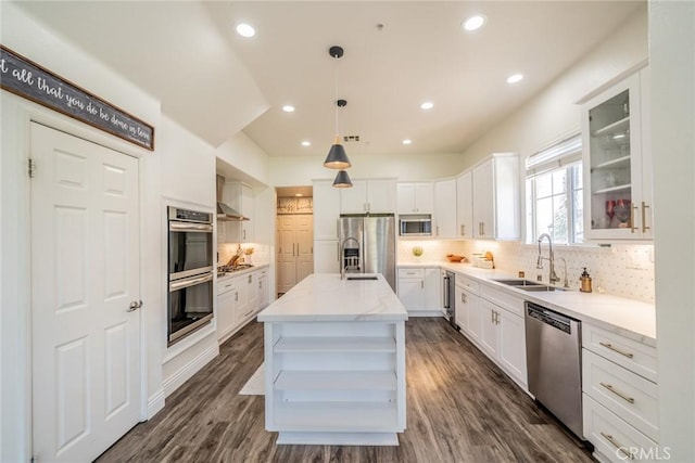 kitchen with appliances with stainless steel finishes, glass insert cabinets, a center island, hanging light fixtures, and a sink