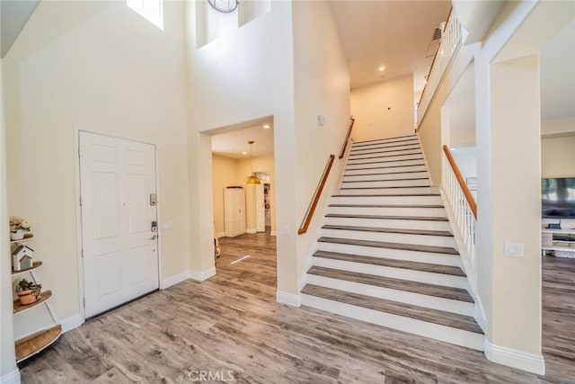 foyer entrance with baseboards, stairway, a towering ceiling, and wood finished floors