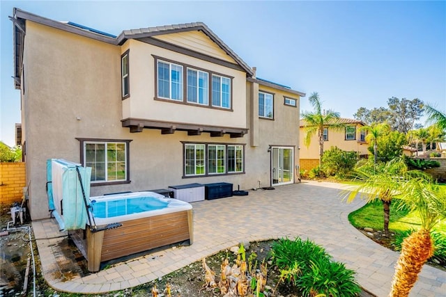 rear view of property with a patio area, a hot tub, fence, and stucco siding