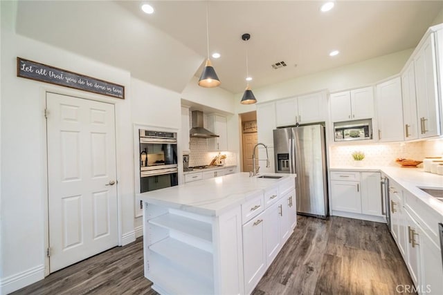 kitchen featuring a sink, white cabinets, appliances with stainless steel finishes, wall chimney exhaust hood, and a center island with sink