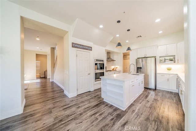 kitchen with a kitchen island with sink, stainless steel appliances, white cabinetry, light countertops, and wall chimney range hood