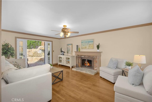 living room featuring ceiling fan, a fireplace, wood finished floors, and crown molding