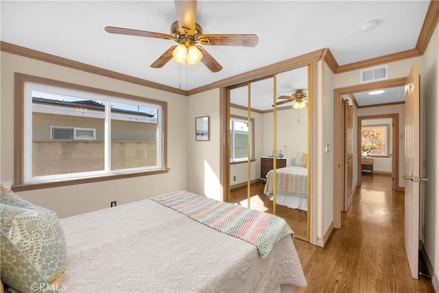 bedroom featuring light wood finished floors, baseboards, visible vents, ornamental molding, and a closet