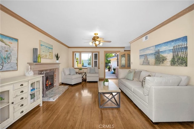 living area with visible vents, ceiling fan, ornamental molding, wood finished floors, and a lit fireplace