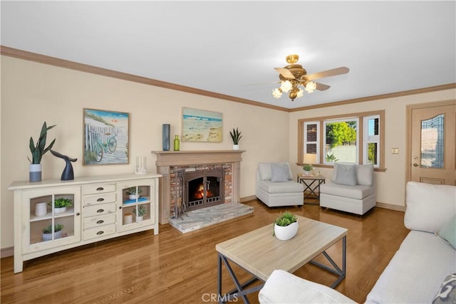 living room featuring a fireplace, crown molding, baseboards, and wood finished floors