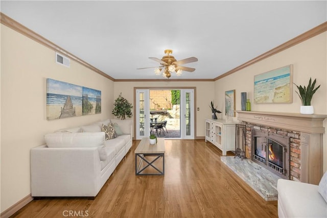 living area featuring a glass covered fireplace, visible vents, crown molding, and wood finished floors