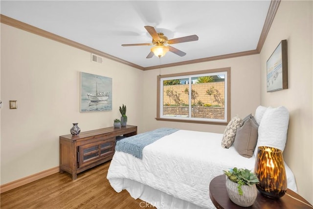 bedroom featuring visible vents, crown molding, baseboards, and wood finished floors